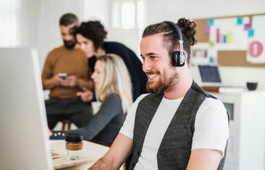 Ein Porträt eines jungen Geschäftsmannes mit Kopfhörern und Kollegen in einem modernen Büro, lachend. - HPIF28151