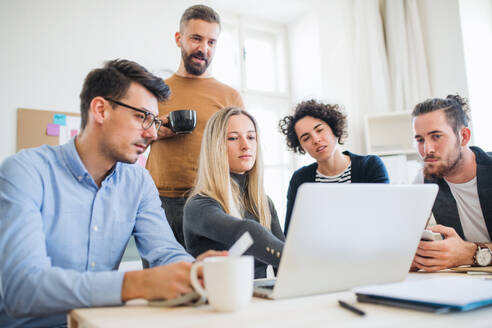 Eine Gruppe junger, fröhlicher Geschäftsleute mit Laptop arbeitet in einem modernen Büro zusammen. - HPIF28154