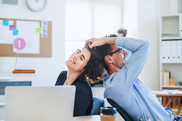 Zwei junge, fröhliche Geschäftsleute entspannen sich in einem modernen Büro und lachen. - HPIF28168