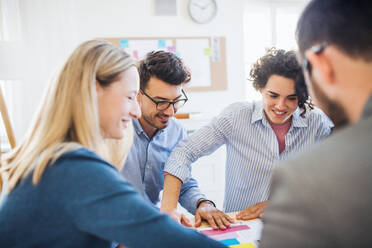 Eine Gruppe junger, fröhlicher Geschäftsleute sitzt in einem modernen Büro um einen Tisch herum und hält eine Besprechung ab. - HPIF28185