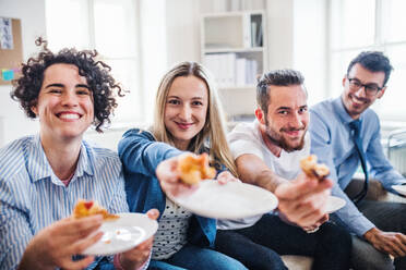 Eine Gruppe von jungen Geschäftsleuten mit Pizza beim Mittagessen in einem modernen Büro. - HPIF28187