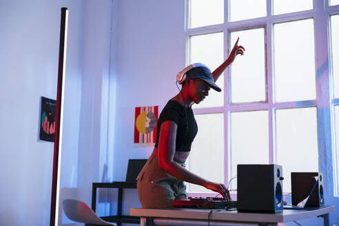 Lächelnder junger DJ mit erhobenem Arm bei der Bedienung des Tonmischers - EBSF03512