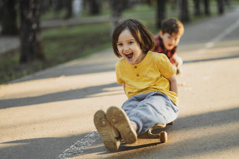 Glückliche Geschwister, die auf der Straße Skateboard fahren - ANAF01490