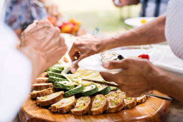 Nahaufnahme von nicht erkennbaren Menschen, die sich Essen auf den Teller legen. Familienfeier im Garten. Großes Gartenfest. - HPIF28193