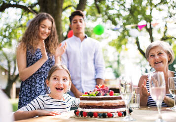 Familienfeier draußen im Garten. Große Gartenparty. Geburtstagsparty. Kleines Mädchen mit Geburtstagstorte. - HPIF28201