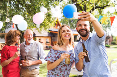 Ein glückliches Paar hält seinen Moment des Glücks in einem Selfie auf einer Party im Freien fest, umgeben von Lachen - HPIF28214