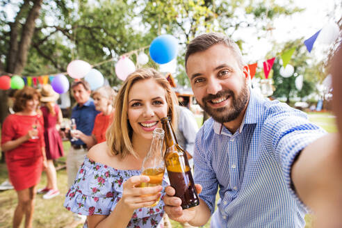 Lächelndes Paar hält Erinnerungen mit einem Selfie fest, während es eine Gartenparty genießt und mit seinen Getränken anstößt - HPIF28215