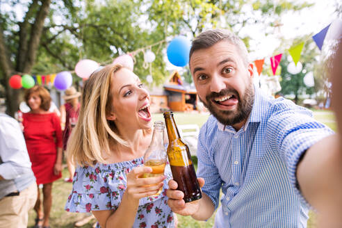 Ein lächelndes Paar, das seine Erinnerungen mit einem Selfie im Garten festhält und sich auf einer Party von seiner verspielten Seite zeigt - HPIF28216