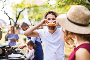 Familienfeier im Hinterhof, Grillparty, ein junger Mann isst einen Hamburger. - HPIF28241