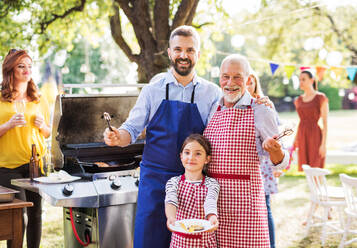 Ein reifer Mann mit Familie und Freunden, der draußen auf einer Grillparty Essen zubereitet. Familienfeier im Hinterhof. - HPIF28243