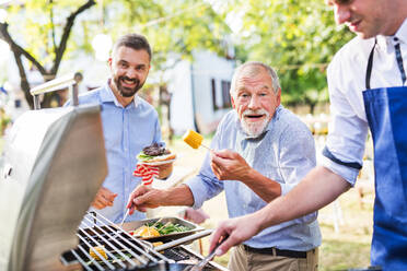 Männer mit Familie und Freunden, die draußen auf einer Grillparty Essen zubereiten. Familienfeier im Hinterhof. - HPIF28247