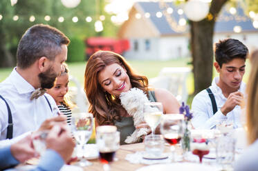 Guests with a small white dog sitting at the table outside in the backyard. - HPIF28257