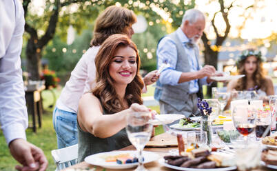 Die Gäste sitzen am Tisch und essen bei der Hochzeitsfeier draußen im Garten. - HPIF28267