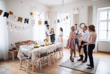 Mehrgenerationenfamilie mit Geschenken, die auf einer Geburtstagsfeier im Haus stehen und sich unterhalten. - HPIF28284