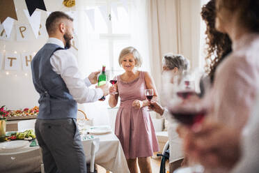 Ein Mann schenkt glücklichen Gästen auf einer Indoor-Familiengeburtstagsfeier Wein ein. - HPIF28288