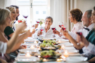 Eine große Familie sitzt an einem Tisch auf einer Indoor-Geburtstagsfeier und stößt mit Rotwein an. - HPIF28291