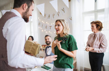 Ein Mann überreicht einer jungen, überraschten Frau ein Geschenk zu einem Familiengeburtstag oder Jahrestag. - HPIF28295