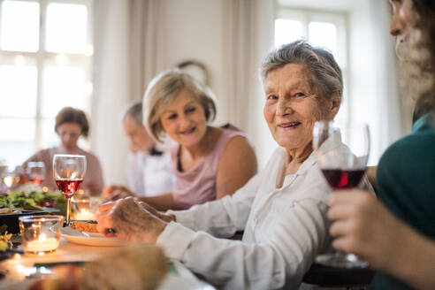 Eine ältere Frau sitzt mit ihrer Familie bei einer Familiengeburtstagsfeier im Haus am Tisch und isst. - HPIF28297