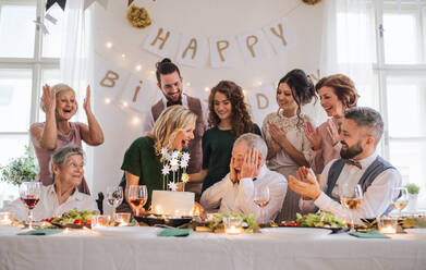 Ein älterer Mann mit einer Mehrgenerationenfamilie und einer Torte feiert seinen Geburtstag auf einer Indoor-Party. - HPIF28298