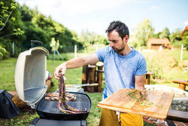 Älterer Mann, der an einem sonnigen Tag im Hinterhof Meeresfrüchte auf einem Grill zubereitet. - HPIF28312