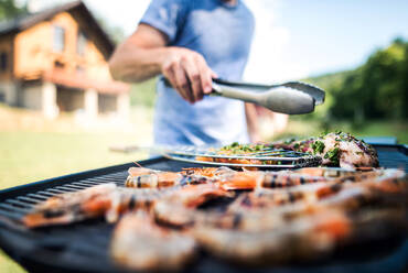 Unrecognizable man cooking seafood on a barbecue grill in the backyard on a sunny day. - HPIF28314