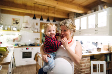Schöne junge schwangere Frau mit einem kleinen Jungen in der Küche zu Hause. - HPIF28328