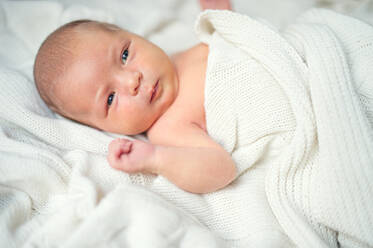 Nahaufnahme eines niedlichen neugeborenen Babys, das auf einem Bett liegt, zugedeckt von einer weißen Decke. - HPIF28333