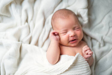 Nahaufnahme eines niedlichen Neugeborenen, das mit einer weißen Decke zugedeckt auf einem Bett liegt, schläft und lächelt, Ansicht von oben. - HPIF28336