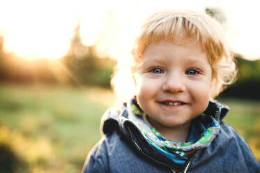 Ein glücklicher kleiner Junge steht bei Sonnenuntergang auf einer Wiese im Freien, Nahaufnahme. - HPIF28351