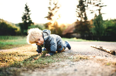 Ein glücklicher kleiner Junge im Kleinkindalter, der bei Sonnenuntergang auf einer Straße herumkrabbelt. - HPIF28352