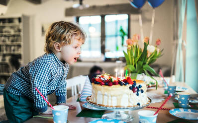 Ein Junge steht auf einem Stuhl und bläst die Kerzen auf einem Geburtstagskuchen aus. Eine Geburtstagsfeier. - HPIF28364