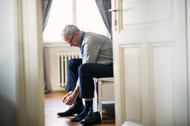 Mature businessman with glasses on a business trip sitting ina hotel room, tying shoelaces. - HPIF28365