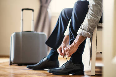 Midsection view of unrecognizable mature businessman on a business trip sitting ina hotel room, tying shoelaces. - HPIF28366