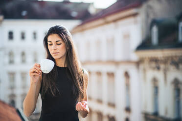 Glückliche junge Geschäftsfrau mit einer Tasse Kaffee auf einer Terrasse vor einem Büro in der Stadt. - HPIF28376