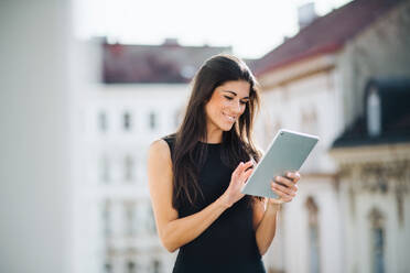 Young businesswoman with tablet standing on a terrace outside an office in city. Copy space. - HPIF28378