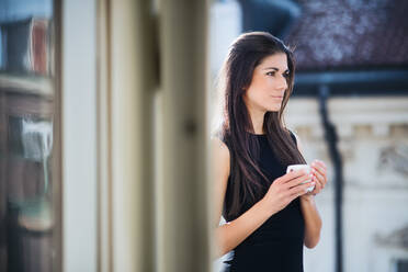 Glückliche junge Geschäftsfrau mit einer Tasse Kaffee auf einer Terrasse vor einem Büro in der Stadt. - HPIF28381