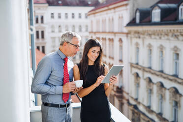Man and woman business partners with tablet standing on a terrace in office in city, talking. - HPIF28385