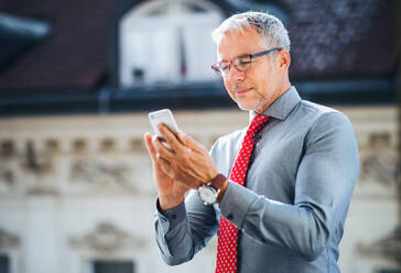 Ein reifer Geschäftsmann mit Smartphone steht auf einer Terrasse in einem Büro in der Stadt und schreibt eine SMS. - HPIF28392