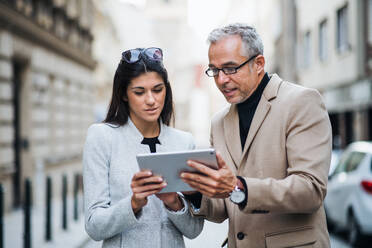 Älterer Mann und junge Frau, Geschäftspartner mit Tablet, stehen im Freien in der Stadt Prag und unterhalten sich. - HPIF28395