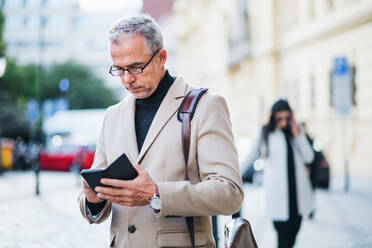 Älterer Geschäftsmann, der auf einer Straße in der Stadt steht und ein Smartphone benutzt. Platz kopieren. - HPIF28398