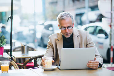 Älterer Geschäftsmann mit Laptop sitzt in einem Café in der Stadt und arbeitet. - HPIF28408
