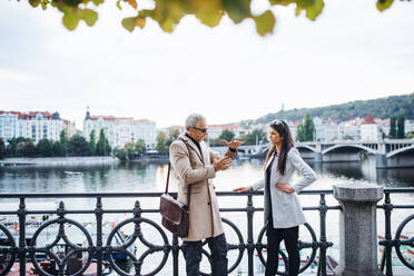 Älterer Mann und junge Frau, die als Geschäftspartner an einem Fluss in der Stadt Prag stehen und sich unterhalten. - HPIF28413
