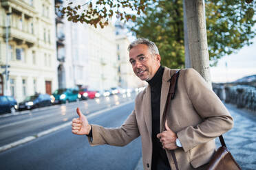 Älterer Geschäftsmann mit Tasche steht auf der Straße in der Stadt Prag und hebt die Hand, um ein Taxi zu rufen. - HPIF28418