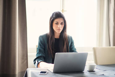 Young beautiful businesswoman sitting indoors at a table, using laptop. - HPIF28431