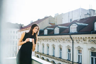 Glückliche junge Geschäftsfrau mit einer Tasse Kaffee auf einer Terrasse vor einem Büro in der Stadt. - HPIF28434