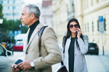 Mature man and young woman business partners walking outdoors in city of Prague. - HPIF28441