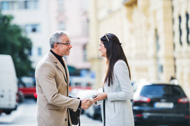 Ein reifer Mann und eine junge Frau stehen als Geschäftspartner im Freien in Prag und schütteln sich die Hände. - HPIF28442