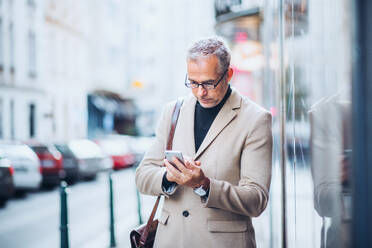 Mature businessman standing on a street in city, holding smartphone. Copy space. - HPIF28443