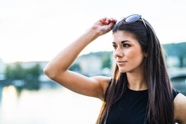 Eine schöne Frau in einem schwarzen Kleid steht an einem Fluss in der Stadt Prag und trägt eine Sonnenbrille. - HPIF28451