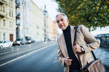Mature businessman with bag standing on the street in city of Prague, waiting for a taxi cab. Copy space. - HPIF28467